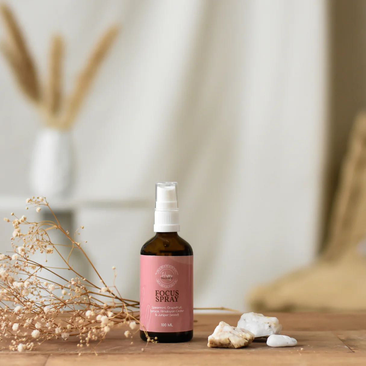 Bruine glazen fles met wit pompje en roze label met de tekst “Focus Spray” van Wasgeluk, gestyled op een houten tafel met droogbloemen en stenen voor een natuurlijke, luxe geurbeleving.