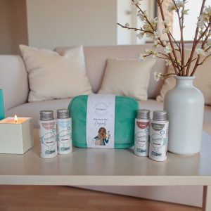 Wasgeluk cadeaupakket met groene pouch en meerdere flesjes duurzame, microplasticvrije wasparfum Essentielle Nature op een salontafel in een stijlvolle, beige woonkamer met brandende kaars en witte vaas met bloemen.