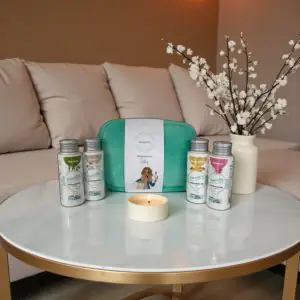 Wasgeluk giftset met turquoise toilettas en meerdere flesjes duurzame, microplasticvrije wasparfum op een ronde witte salontafel met brandend kaarsje en bloesemtak, voor een luxe en langdurige geurbeleving in huis en was.