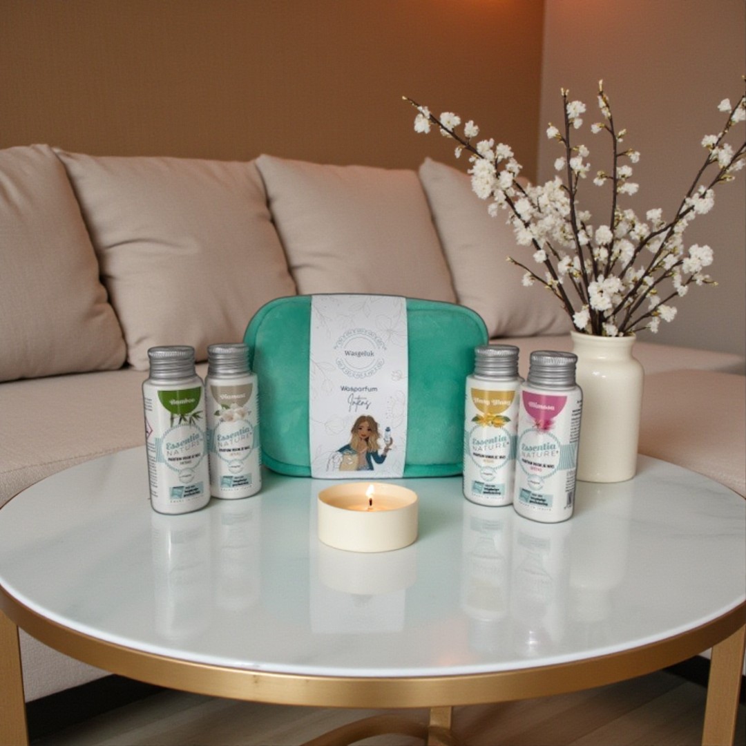 Wasgeluk giftset met turquoise toilettas en meerdere flesjes duurzame, microplasticvrije wasparfum op een ronde witte salontafel met brandend kaarsje en bloesemtak, voor een luxe en langdurige geurbeleving in huis en was.