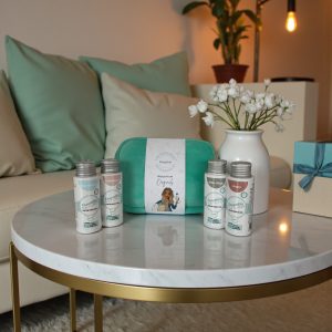 Wasgeluk wasparfum giftset op een marmeren salontafel met turquoise toilettas en vier flesjes Zaai met die Natuur wasparfum, omringd door pastelkleurige kussens en een vaas met witte bloemen voor een luxe, duurzame geurbeleving.