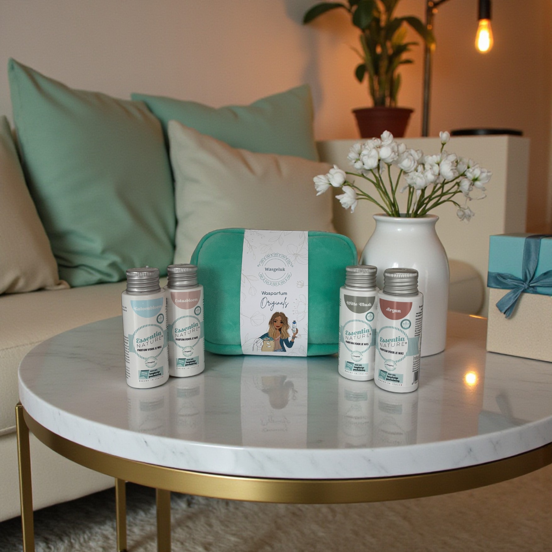 Wasgeluk wasparfum giftset op een marmeren salontafel met turquoise toilettas en vier flesjes Zaai met die Natuur wasparfum, omringd door pastelkleurige kussens en een vaas met witte bloemen voor een luxe, duurzame geurbeleving.